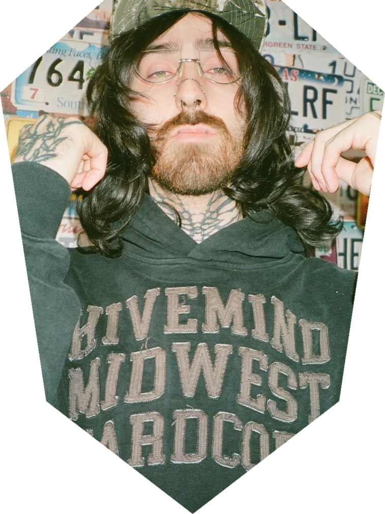 Quinn photographed in front of a wall of license plates, cropped into a coffin shape.